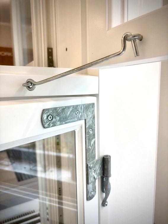 Ein Sturmhaken mit traditionellem fensterbschlaf an einem nach aussen öffnendem Fenster aus Holz.