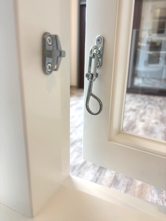 Ein alter traditioneller Ankettel-Verschluss an einem weißen Holzfenster nach aussen öffnend.