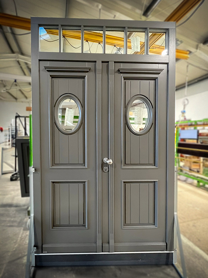 Zweiflüglige Hauseingangstür mit ovalen Fenstern und Zierelementen in Grau